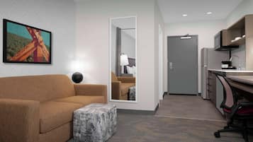 A modern hotel room with a sofa, ottoman, and a large mirror.