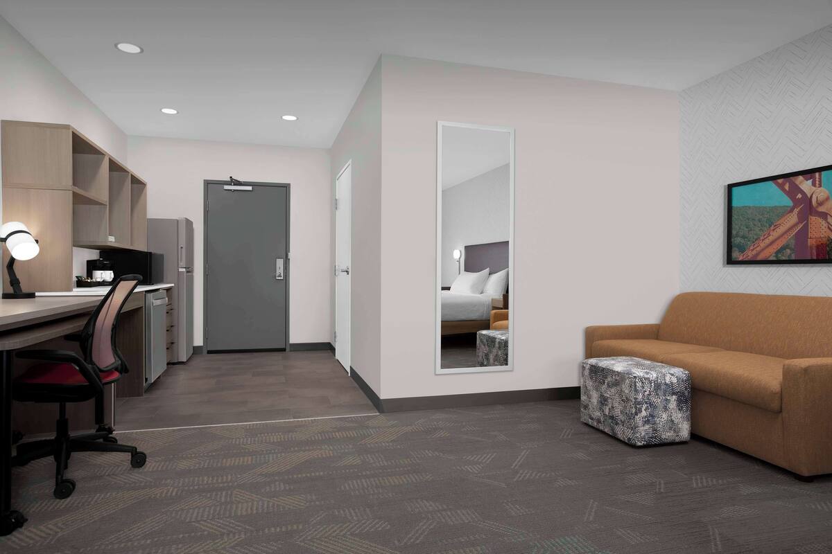 A hotel room with a desk, office chair, sofa, ottoman, and a large mirror.