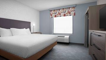 Quarto de hotel com cama, escrivaninha, televisão e janela com cortina.