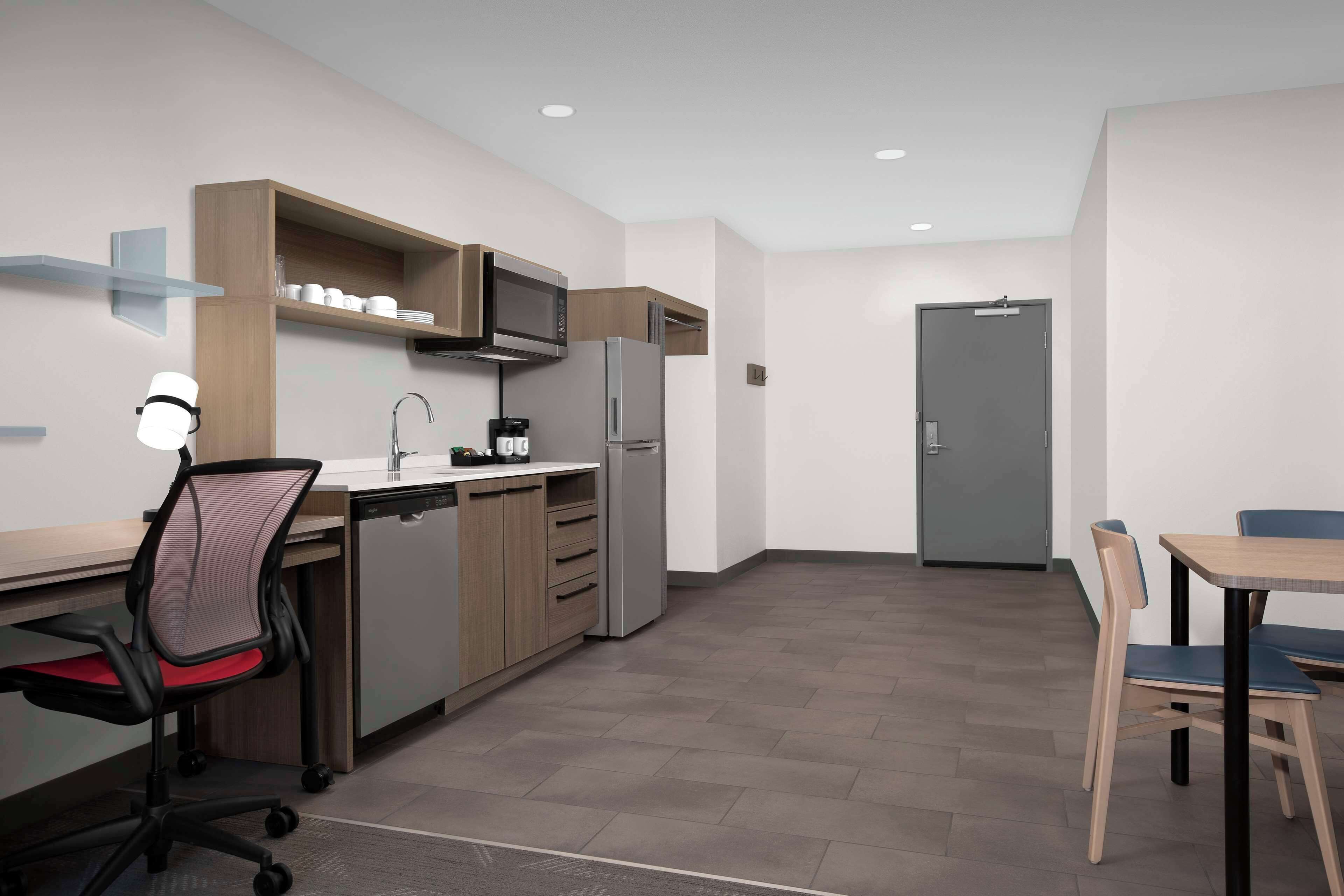 Una cocina moderna con microondas, refrigerador y cafetera. Hay un escritorio con una silla y una mesa de comedor con sillas.