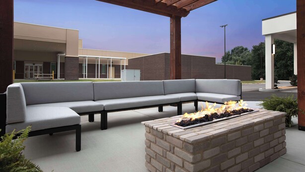 An outdoor seating area with a brick fire pit and a grey sofa under a wooden pergola. - Home2 Suites By Hilton Chattanooga East Ridge (Chattanooga)