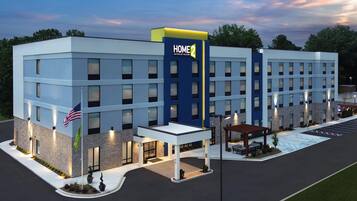 Un hotel moderno con un llamativo letrero 'HOME 2', múltiples accesos y una zona de estacionamiento bien iluminada.