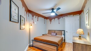 Una camera da letto con un letto, una ventola a soffitto, un comodino, una lampada e una porta.