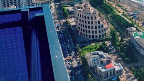 Paesaggio costiero con grattacieli, un edificio storico circolare e una spiaggia.