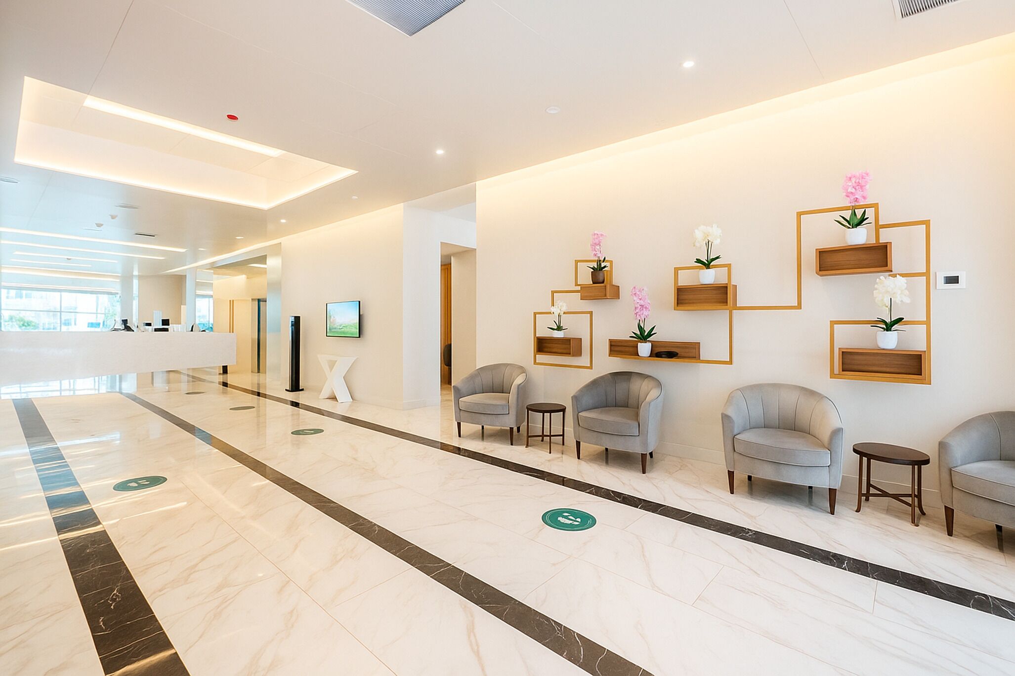 Un moderno vestíbulo de hotel con suelo de mármol, sillones grises y estanterías de madera con plantas en macetas.