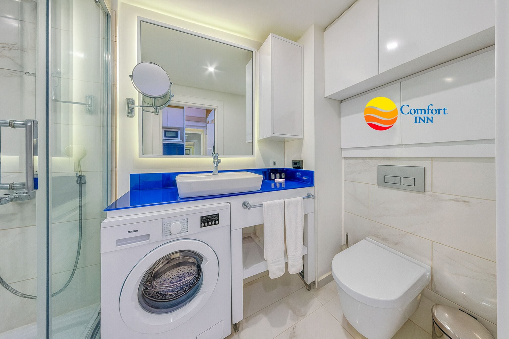 A modern bathroom with a washing machine, a sink, a toilet, and a glass shower enclosure.