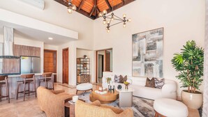 A spacious living area with a modern kitchen, a white sofa, and a large abstract painting.