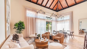 A spacious living area with a high ceiling, a round wooden coffee table, and a large potted plant.