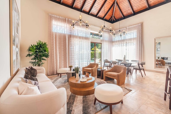 A spacious living area with a high ceiling, a round wooden coffee table, and a large potted plant.