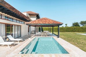A modern house with a swimming pool, outdoor seating, and a covered patio.