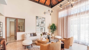 A spacious living room with a white sofa, round coffee table, and wicker armchairs. A large mirror and abstract art are on the walls.