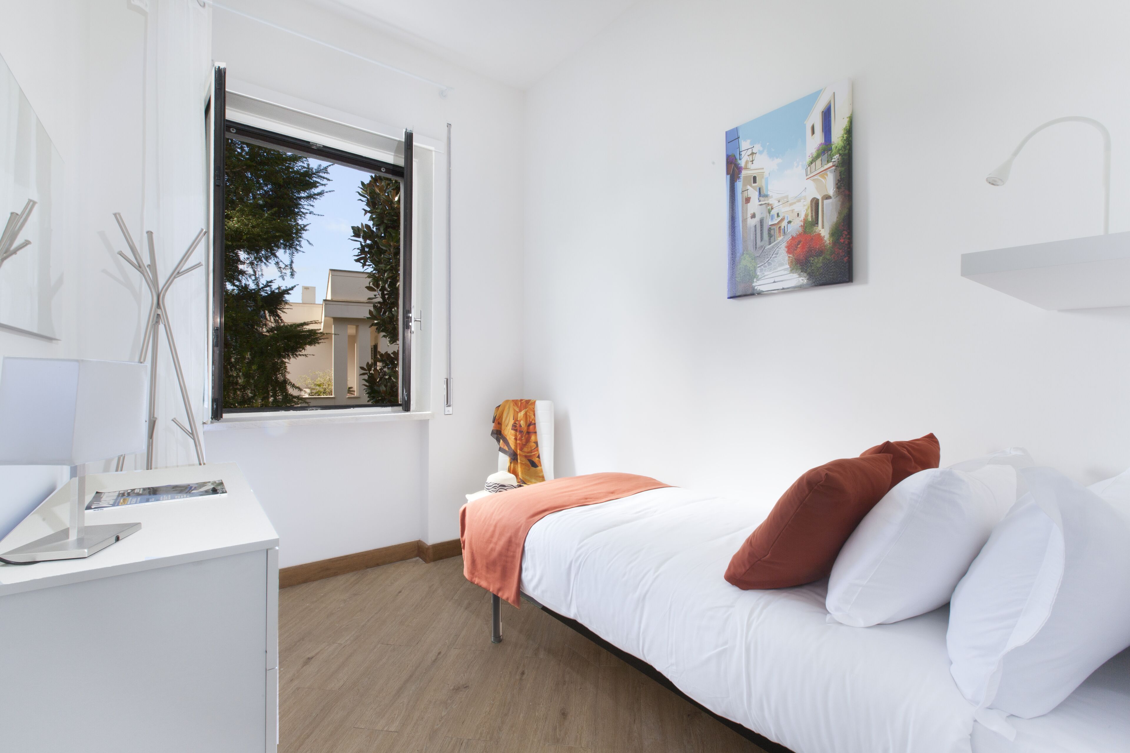 Un dormitorio moderno con cama, escritorio, ventana y un cuadro en la pared.