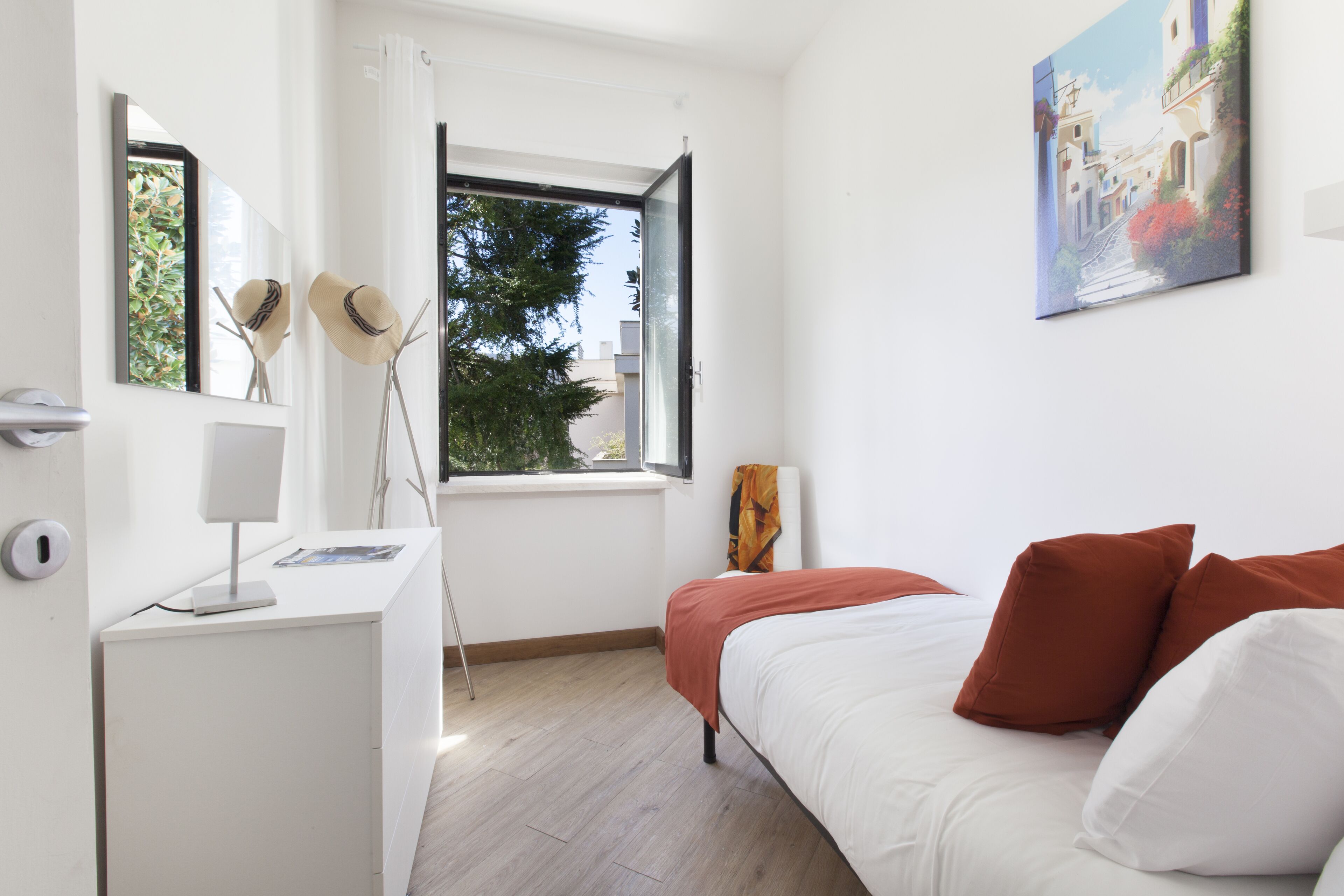 A bedroom with a bed, a desk, a chair, a window, and a painting on the wall.