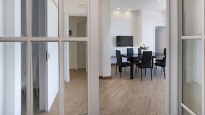 A modern dining area with a glass partition, a flat-screen TV, and a potted plant.