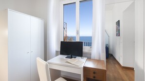 A modern bedroom with a desk, a chair, a wardrobe, and a window with a view of the sea.