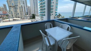 Ein Balkon mit einem weißen Tisch und Stühlen, der auf eine Stadtlandschaft mit hohen Gebäuden und Blick auf das Meer blickt.