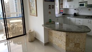 Eine moderne Küche mit Granitarbeitsplatte, weißen Schränken und Blick auf die Stadt durch eine Schiebetür.