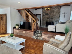 A living room with a stone fireplace, a wooden staircase, a flat-screen TV, and leather furniture. - Relax near Gettysburg ski/wineries/fire pit! (Orrtanna)