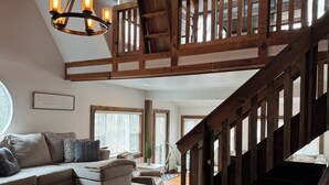 Un'ampia zona giorno con soffitto in legno a vista, una scala e un'ampia finestra che lascia entrare luce naturale.