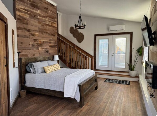 A bedroom with a wooden bed, a staircase, a chandelier, a potted plant, and a TV mounted on the wall. - Relax near Gettysburg ski/wineries/fire pit! (Orrtanna)