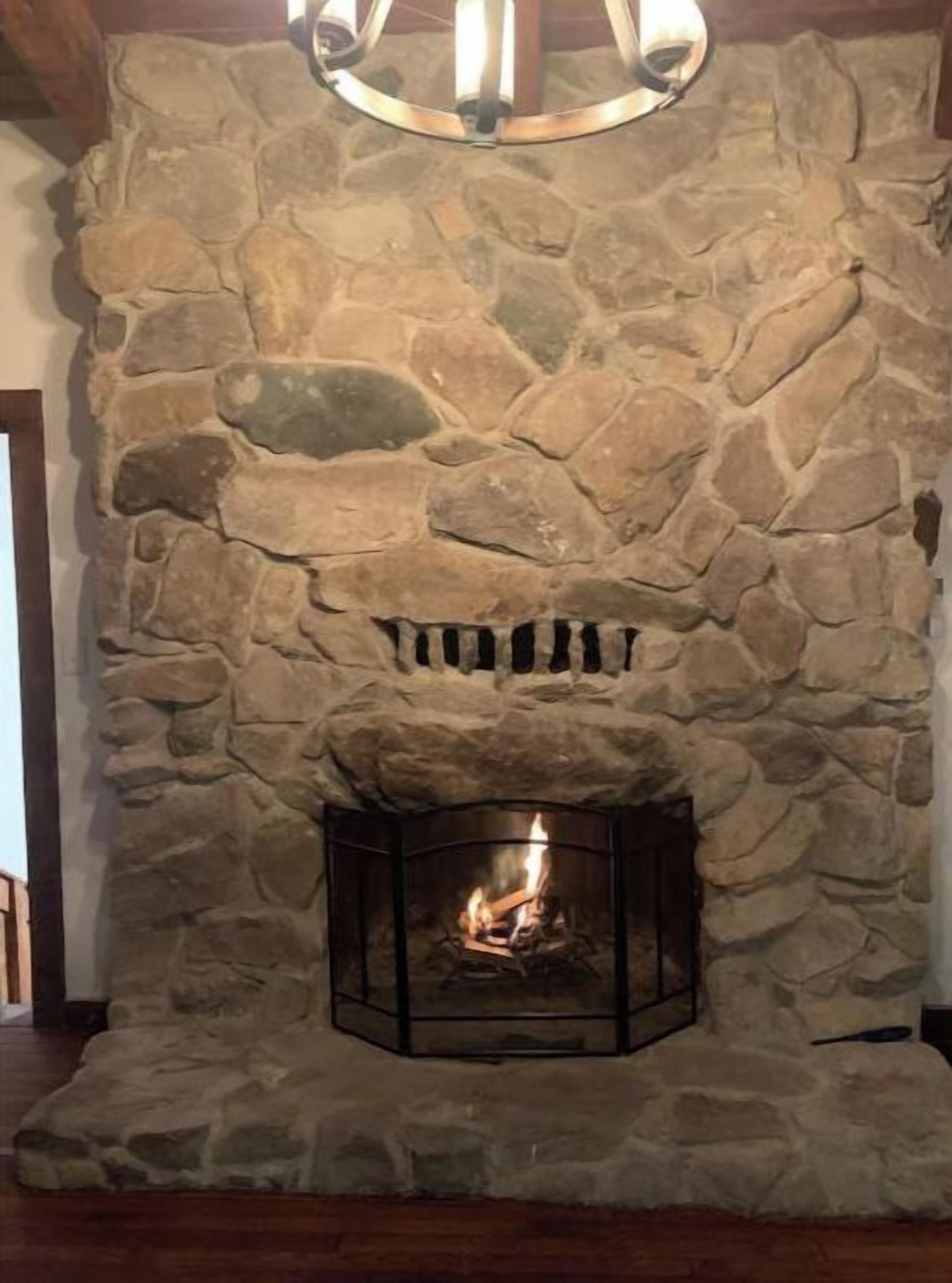 Una chimenea de piedra con fuego encendido, un repisa de madera y un muro de piedra arriba.