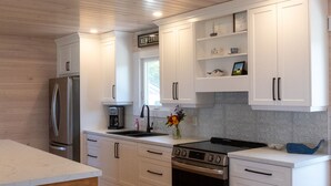 A modern kitchen with white cabinets, stainless steel appliances, and a wooden floor. - Saltwater Song Beach House (New London)