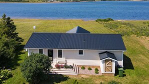 A house with a dark roof, white exterior, and a front porch with a bench and potted plants. - Saltwater Song Beach House (New London)