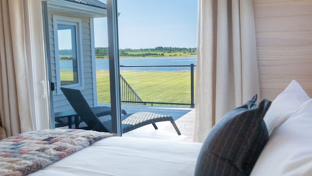 A bedroom with a bed, a view of a balcony, and a door leading to an outdoor area. - Saltwater Song Beach House (New London)