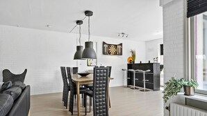 Un salon moderne avec un coin repas, comprenant un canapé en cuir noir, une table à manger en bois avec des chaises et un luminaire suspendu noir.