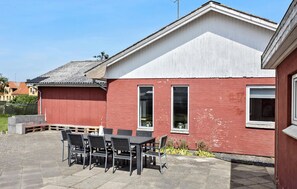 A red building with a white roof, a patio with a table and chairs, and a small garden area. - Lovely home in Vestervig with kitchen (Vestervig)