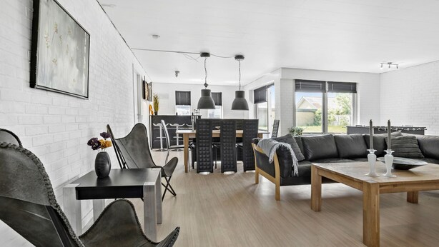 Un salon moderne avec coin repas, caractérisé par un mur en briques blanches, des meubles en cuir noir et une table basse en bois.