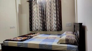 A bedroom with a bed, a patterned bedspread, and a curtain.
