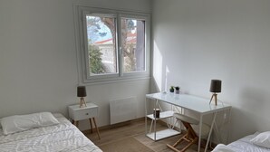 A bedroom with two beds, a desk, and a window.