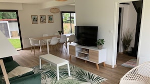 A modern living room with a flat-screen TV, white furniture, and a large green leaf-patterned rug.