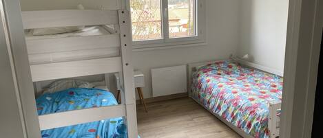 Une chambre avec un lit superposé, un lit simple recouvert d’une courtepointe à motifs floraux, une fenêtre et un radiateur.