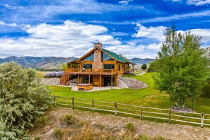 A large, two-story log cabin with a stone chimney, a covered porch, and a well-maintained lawn.