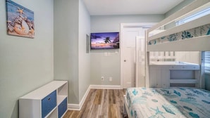 A bedroom with a bunk bed, a flat-screen TV mounted on the wall, and a small cabinet with drawers.