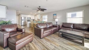 A spacious living room with a brown leather sofa set, a coffee table, and a dining area with a wooden table and chairs.