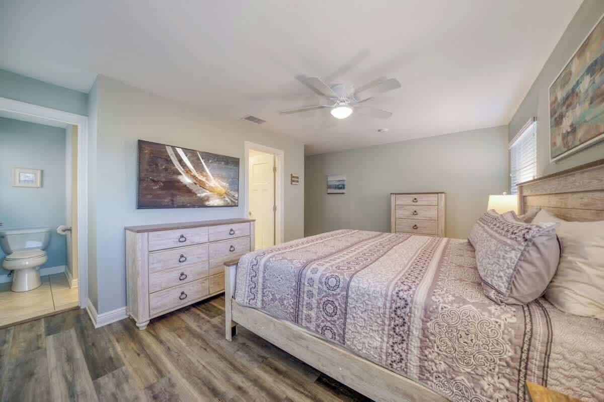 A bedroom with a bed, a dresser, a ceiling fan, and a painting on the wall.