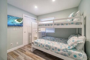 Une chambre avec un lit superposé, une couette aux motifs marins, une porte et un tableau accroché au mur.