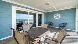 A covered outdoor seating area with a table and chairs, a view of the ocean, and a logo on the wall.
