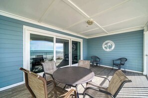 A covered outdoor seating area with a table and chairs, a view of the ocean, and a logo on the wall. - Four Shores #3 Gulf Condo Direct Gulf w Pool & Spa (Indian Shores)