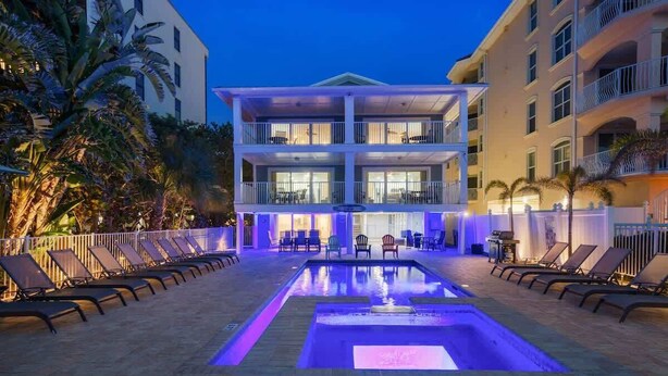 Un hôtel doté d’une piscine, de chaises longues et d’un bâtiment à deux étages avec des balcons.