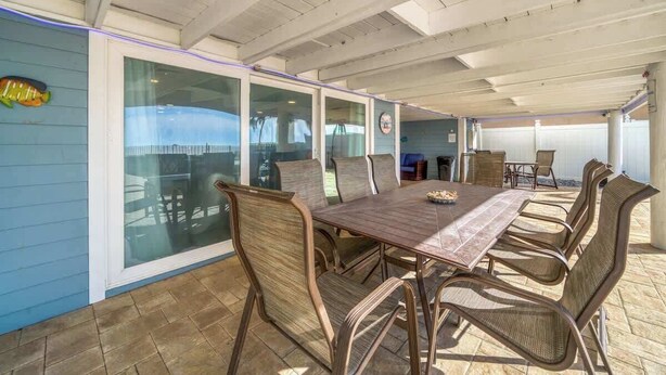 An outdoor patio with a wooden table and chairs, a glass door leading to a pool, and a view of the ocean. - Four Shores #2 Sunset Condo Direct Gulf w Pool&Spa (Indian Shores)