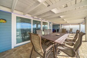 An outdoor patio with a wooden table and chairs, a glass door leading to a pool, and a view of the ocean.