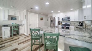 A modern kitchen with white cabinetry, a marble countertop, and a central island with seating. - Four Shores #2 Sunset Condo Direct Gulf w Pool&Spa (Indian Shores)