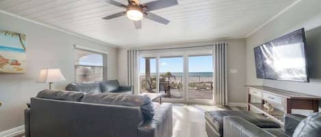 A modern living room with a grey sofa set, a flat-screen TV, and a ceiling fan.
