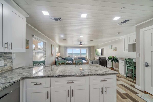 A kitchen with white cabinets, a marble countertop, and a dining area with a view.