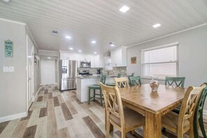 A modern kitchen with white cabinets, a central island, and green chairs around a wooden dining table.