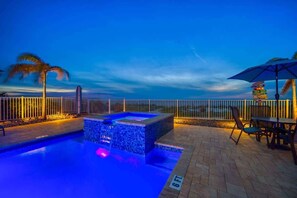 Una piscina con hidromasaje, una mesa con sillas y vista al océano al atardecer.